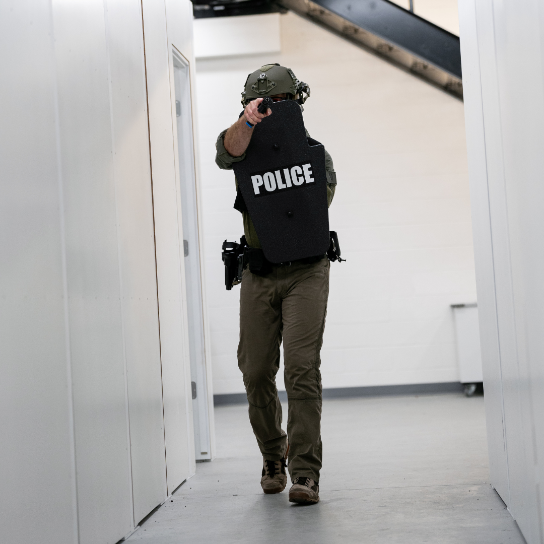 Police officer with a Caliber Armor ballistic shield and pistol clearing a hallway during a tactical operation.