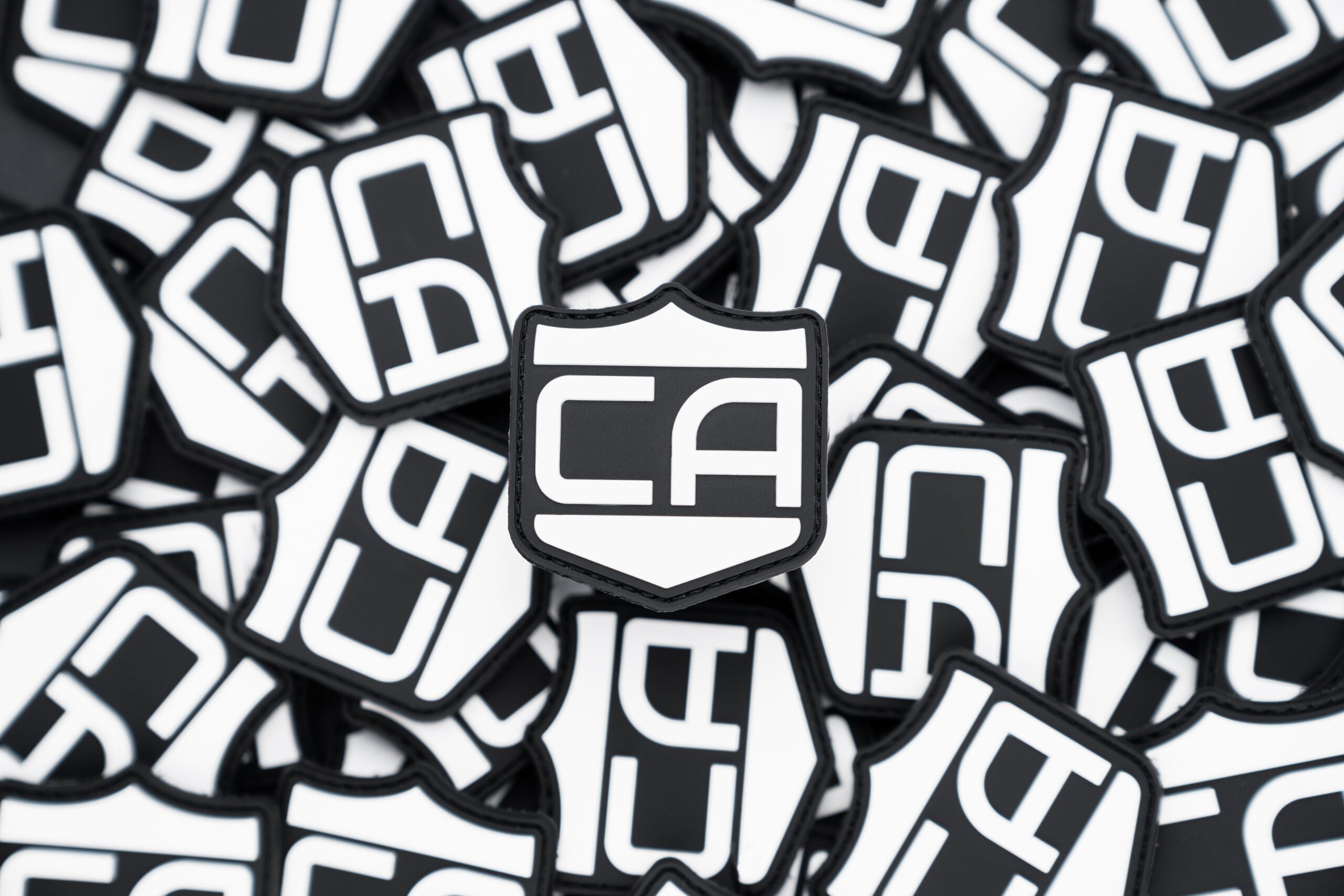 a pile of pvc patch with velcro backing that is the Caliber Armor logo in white with the background being black